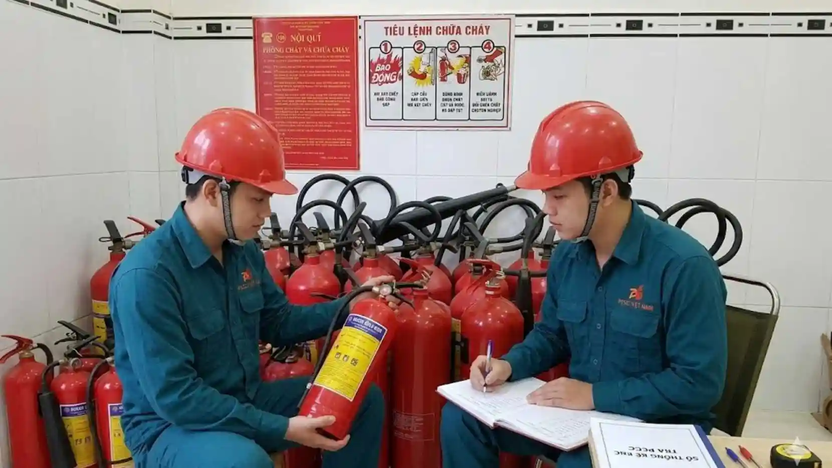 Hai nhân viên đang ghi chép thông số và kiểm tra tình trạng các bình chữa cháy xách tay định kỳ.